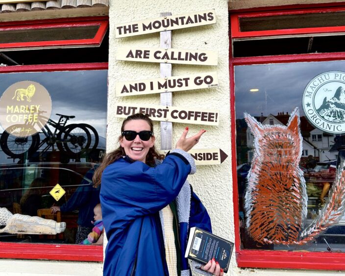 Annabel Wilson pointing to a local business shop window, while smiling in to the camera