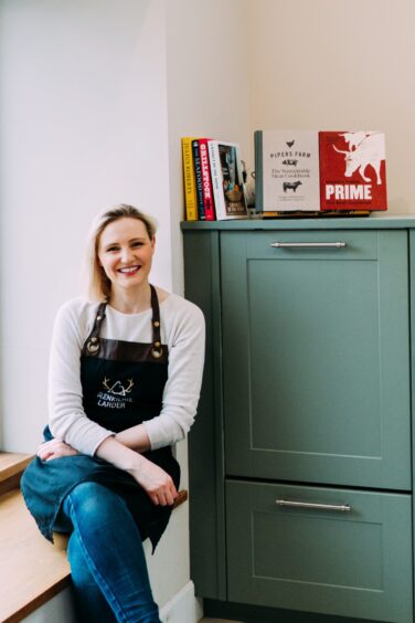 Lauren Houstoun smiling beside window with cookbooks on shelf behind her