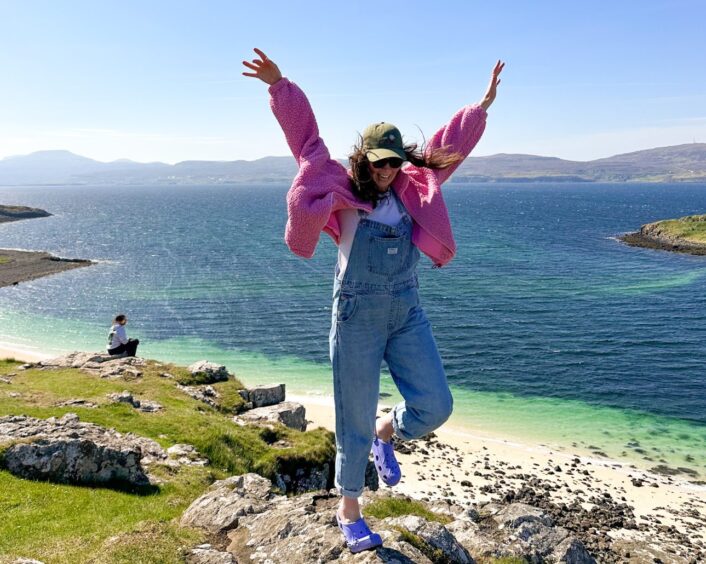 Anabel Wilson with her arms outstretched walking along the beach on a sunny day.