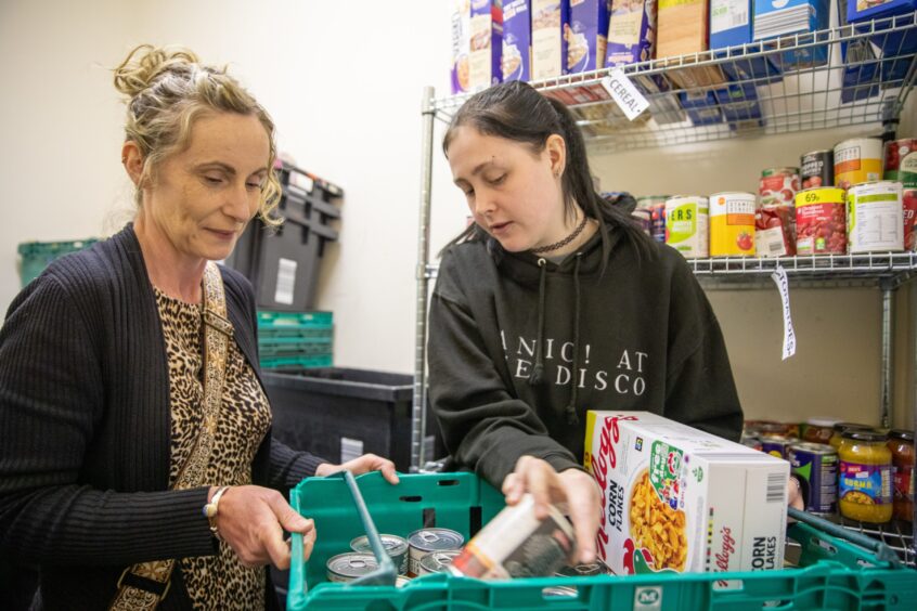 Volunteer Joana Barron shows Cheryl how foodbank parcels are packed.