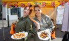 Two women in khaki holding plates of food in front of stall at Perth VE day event