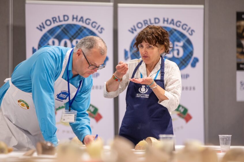 Morag Lindsay making face as Jon Wilkin leans over writing on piece of paper on table covered in haggises