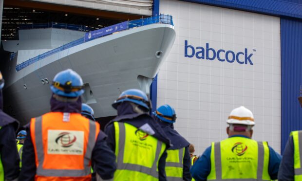 workers watch a new frigate rolling out of a hangar at Rosyth dockyard