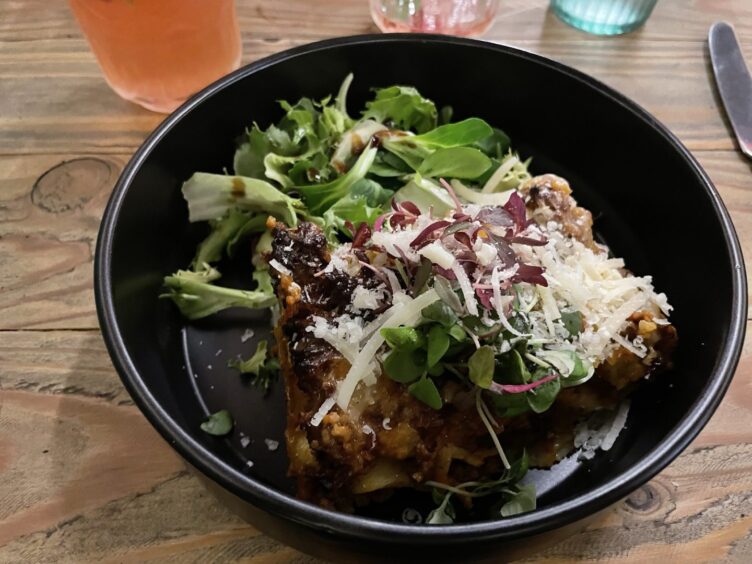 A black dish containing lasange and a pile of fresh salad.