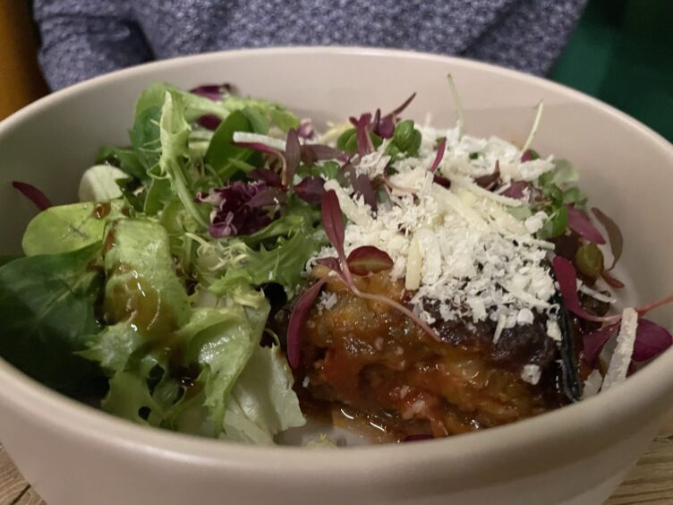 A white dish containing aubergine parmigiana and a pile of fresh salad leaves.