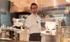 The chefs at work in the open kitchen at The road Hole Restaurant. A chef smiles at the camera in front of a copper-lined commercial kitchen.