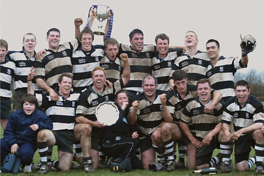 Perthshire rugby team celebrate winning the title. One player is holding up a cup and another a shield