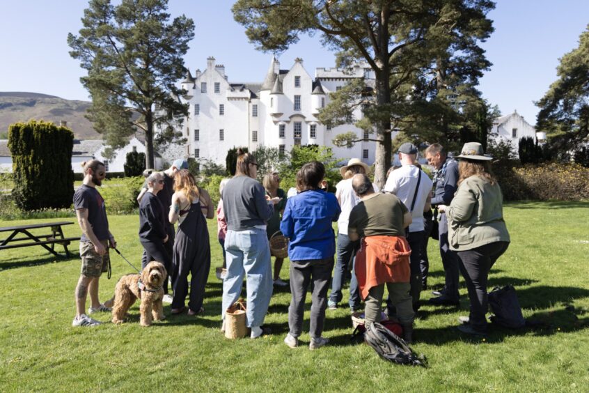 A gorup of people stand on a lawn in front of Blair Castle - a white turreted building.