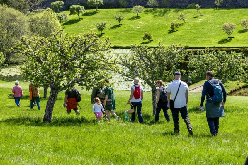 A group walks into the walled garden at Blair Castle with it's pond in the background.