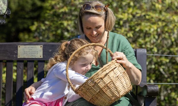 A blond woman and a young girl in a pink dress sit on a bench and look in a wicker basket.
