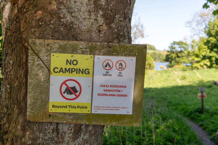 Sign on tree saying 'no camping beyond this point' with Loch of Clunie in distance