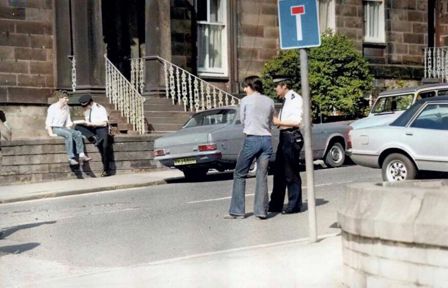 Two police officers speak to two men in Roseangle in May 1980.