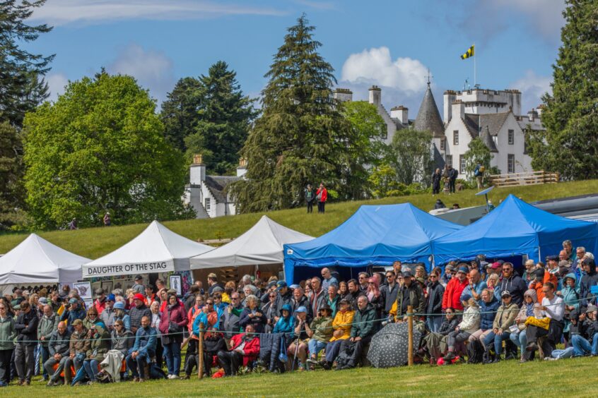 People watching highland games with Blair Castle on hill behind them
