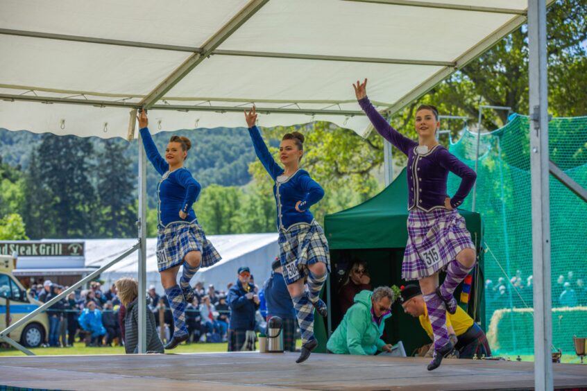 Three girls doing traditional Highland dancing on stage at Atholl Gathering