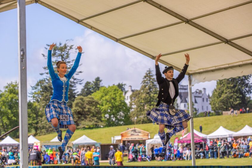 Two people doing Highland dancing on stage with Blair Castle behind