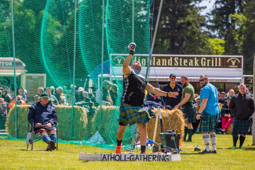 Man throwing shott putt watched by other athletes in kilts