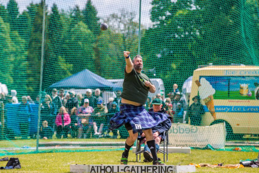 Man in kilt throwing shot putt next to Atholl Gathering sign