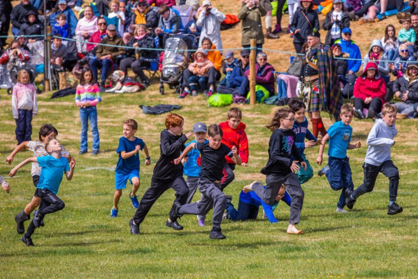 Small boys in regular clothes running watched by crowd around arena at 