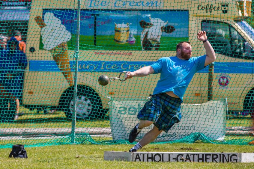 Man in kilt throwing heavy metal weight on chain in front of ice cream van
