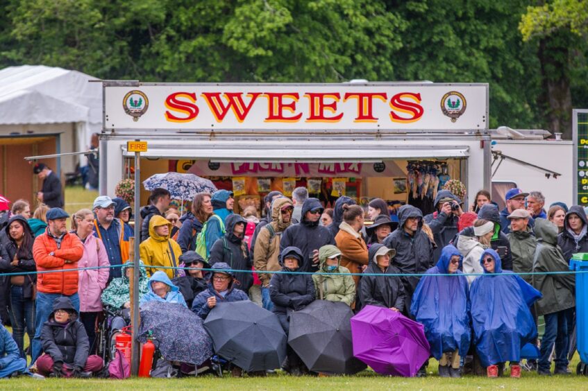 Crowd watching highland games from behind umbrellas wearing waterproof jackets