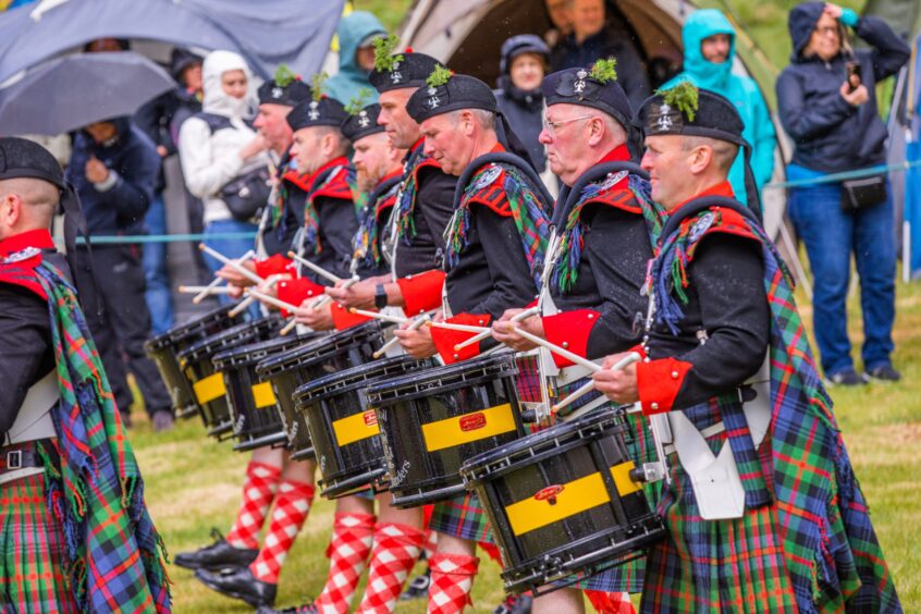 Pipe band members playing drums in formation watched by crowd
