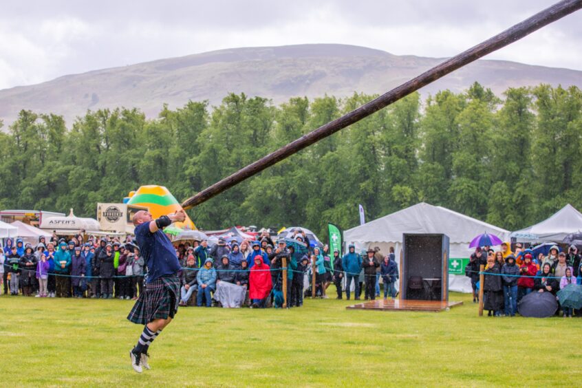 Man tossing caber watched by large crowd in rain