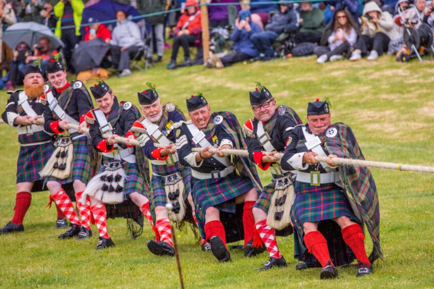 Men in highland dress pulling on rope in tug o war contest watched by crowd at Atholl gathering