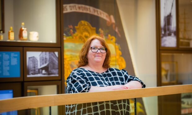 Helen Smout, smiling, in front of display cases at Perth Museum