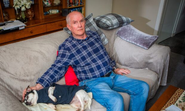 Norman Hawkes seated on sofa with small dog lying beside him