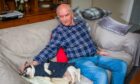Norman Hawkes seated on sofa with terrier sleeping beside him.