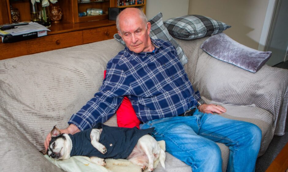 Norman Hawkes seated on sofa with terrier sleeping beside him.