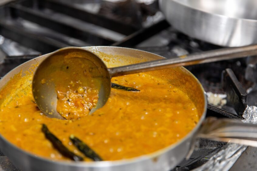 A silver pan of orangey dal with whole chillies floating in it.
