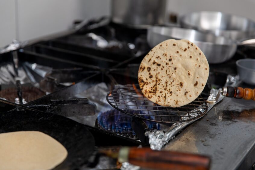 A chapati is cooked directly on the flame of a commercial hob.