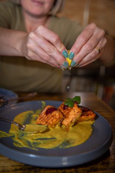 A lady squeezes a lemon wedge onto a dish on tandoori salmon.