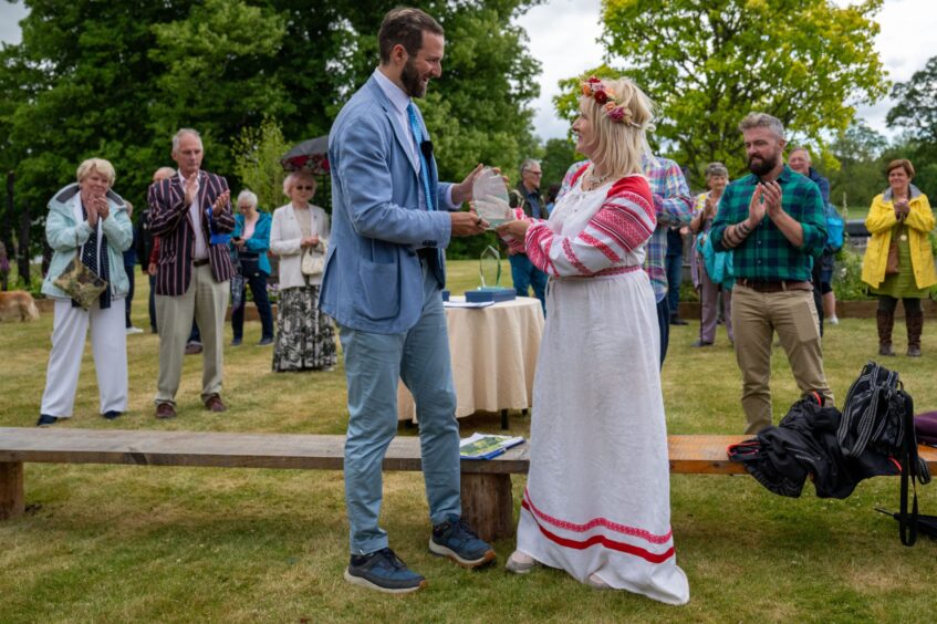 Viscount Stormont presenting prize to woman in long white dress watched by applauding crowd