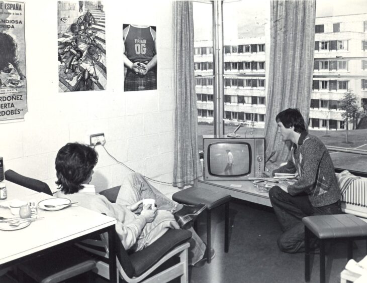 Image shows: a black and white picture of a student lounge where two students are watching TV.