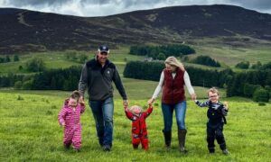 Lauren and Andrew Houstoun walking through field hand in hand with three small children