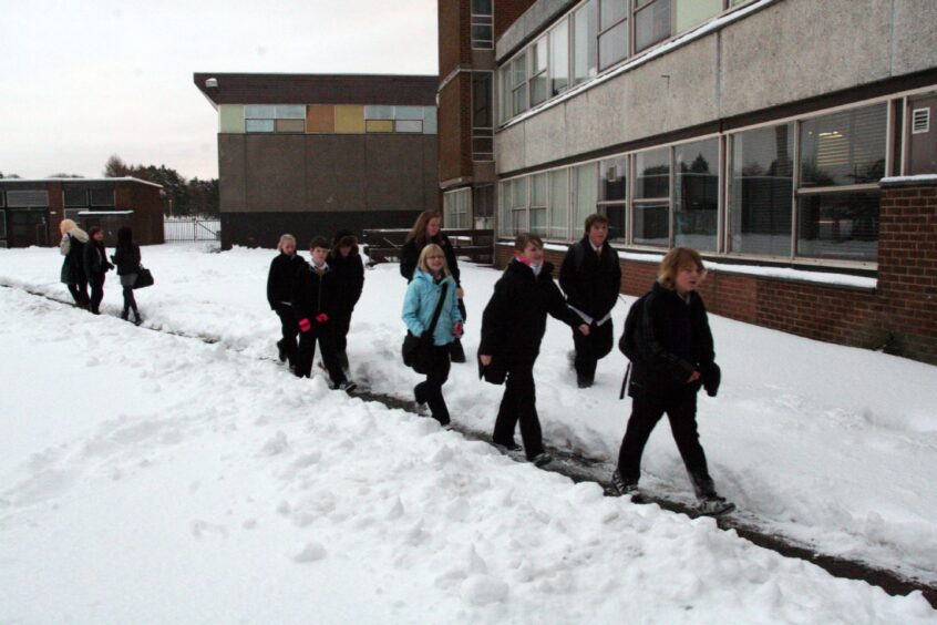 Pupils walking along the path to school that has been cleared through the snow 