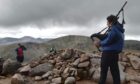 Joel Davey atop a Munro, playing his favourite song Highland Cathedral. Image: Joel Davey