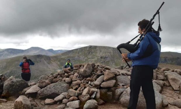 Joel Davey atop a Munro, playing his favourite song Highland Cathedral. Image: Joel Davey
