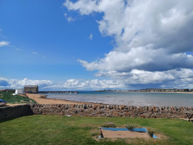 some grass and a stone wall in the foreground and Elie beach. in the background