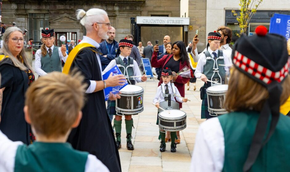Young drummers perform as graduates walk by. 