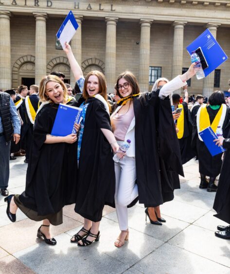 Three female graduates celebrate outside Caird Hall. 