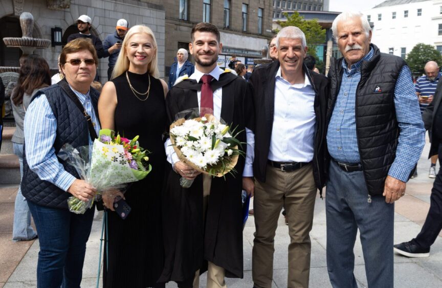 A male graduate flanked on either side by proud friends and family members. 