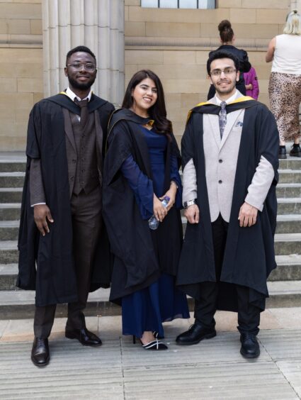 Three graduates pose at the Caird Hall steps. 
