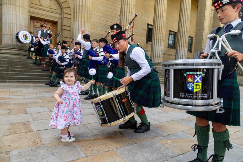 A toddler helps a young drummer with playing duties. 
