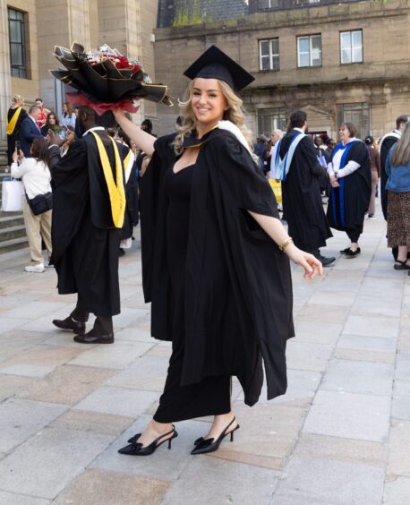 A female graduate smiling with a bouquet.