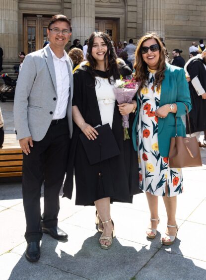 A female graduate with a bouquet, flanked by a man and woman. 