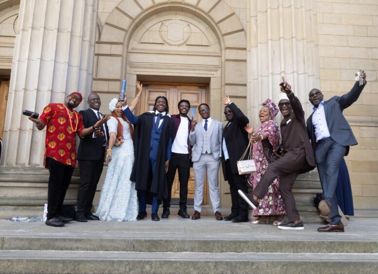 A male graduate flanked on either side by proud friends and family members. 
