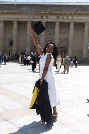 A female graduate poses outside Caird Hall. 